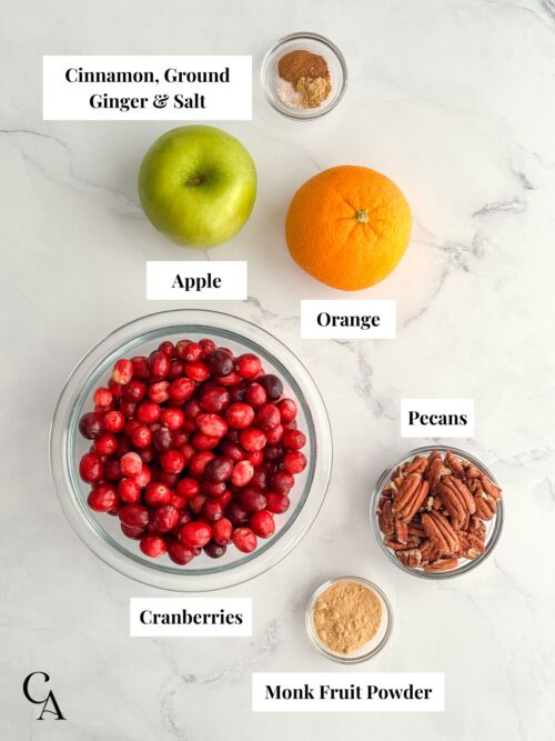 Flat lay of ingredients for cranberry orange relish, including cranberries, apple, orange, pecans, monk fruit powder, cinnamon, ginger, and salt.