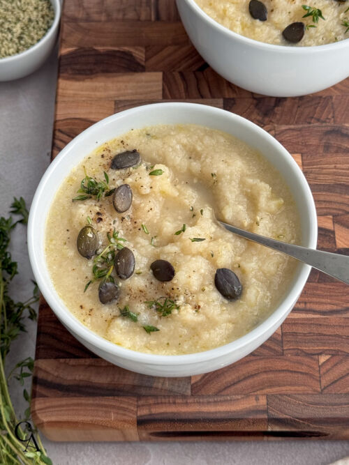 Close-up of a white bowl of soup topped with hemp, thyme, and cracked black pepper.