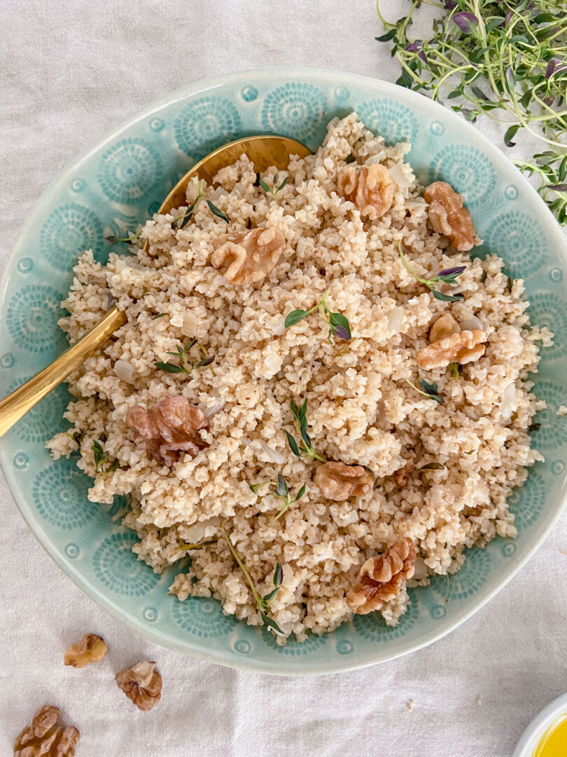 Cooked millet and a gold serving spoon in a large green serving bowl.