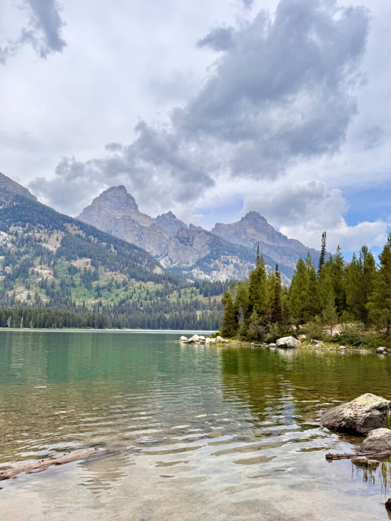 A lake with fir trees and rocky mountains in the distance.