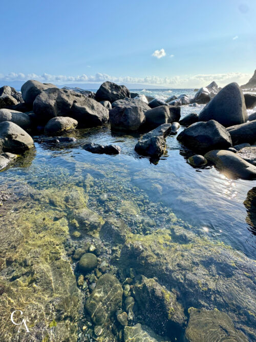 A tide pool with black rocks along a rocky coastline.