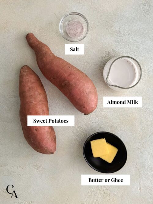 Flat lay of ingredients: raw sweet potatoes, almond milk, sea salt, and butter on a light background with labeled callouts.