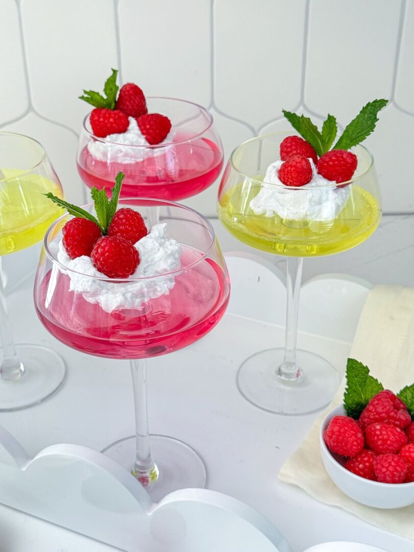 Three servings of sugar-free jello topped with whipped coconut cream and fresh red raspberries in tall dessert glasses.