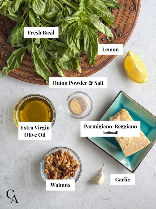 Ingredients for pesto including fresh basil, olive oil, garlic, lemon, walnuts, and Parmigiano-Reggiano.