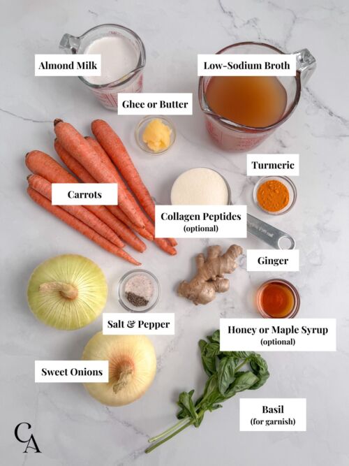 Labeled soup ingredients on a countertop, including carrots, sweet onion, fresh ginger, turmeric, broth, almond milk, maple syrup, salt, and pepper.