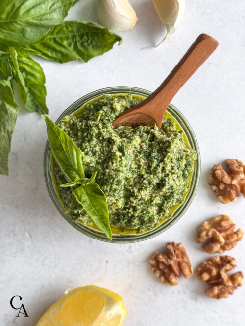 A bowl of homemade pesto sauce with walnuts and a wooden spoon.