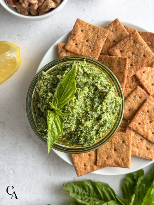 Dairy-free pesto served as a dip with crackers on a white plate.