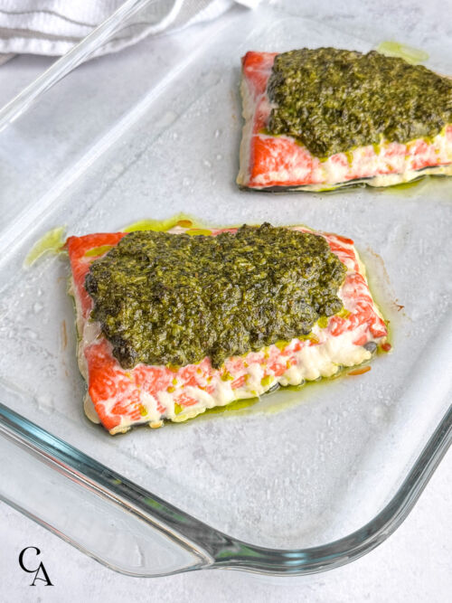 Salmon topped with pesto sauce in a glass baking dish, just after cooking.