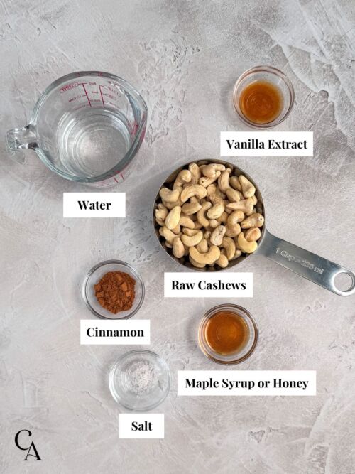 Overlay of ingredients in small bowls and measuring cups, including cashew nuts, cinnamon, maple syrup, vanilla and salt.