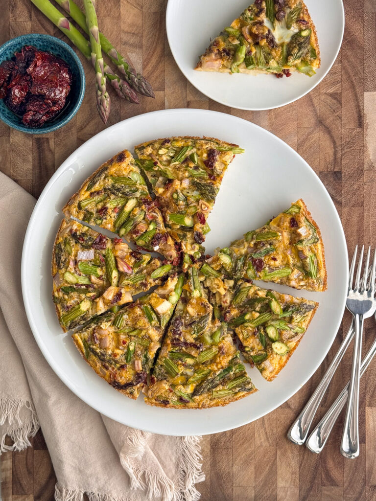 A sliced asparagus frittata with chopped onions and tomatoes on a white plate.