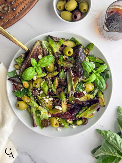 A green salad with olives, asparagus, fresh basil and sun-dried tomatoes sprinkled with feta cheese crumbles.