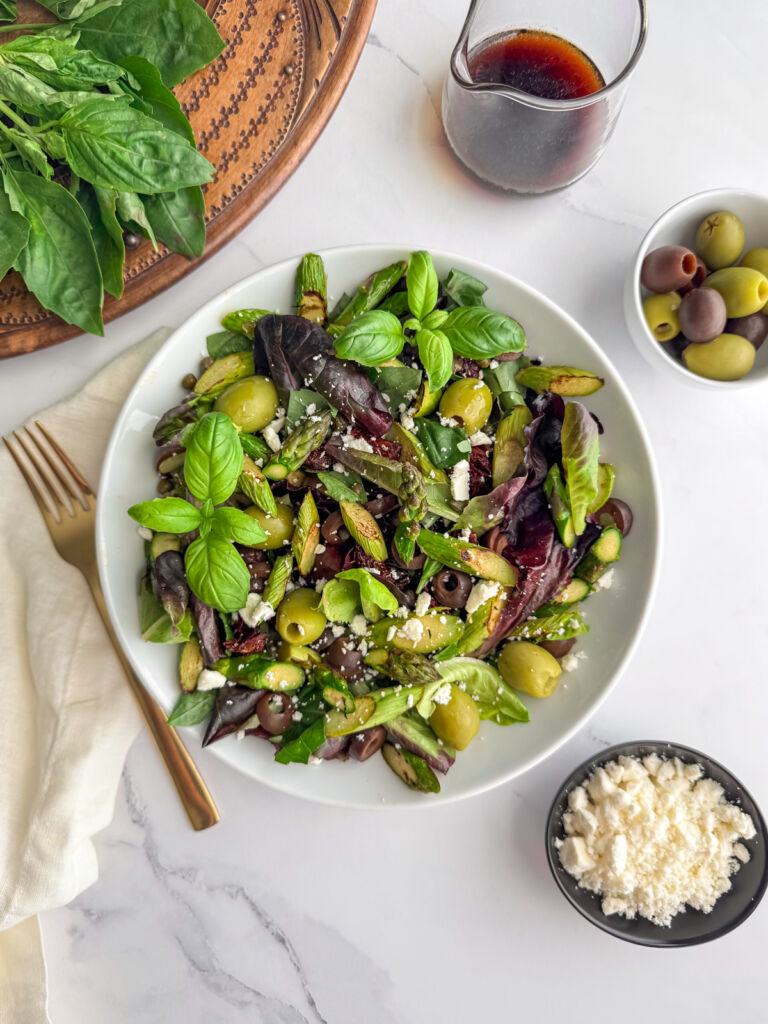 A Mediterranean salad in a white bowl with bowls of olives and feta cheese next to it.