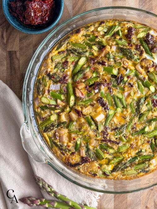A baked frittata in a glass dish with golden edges, resting on a dark wood cutting board.