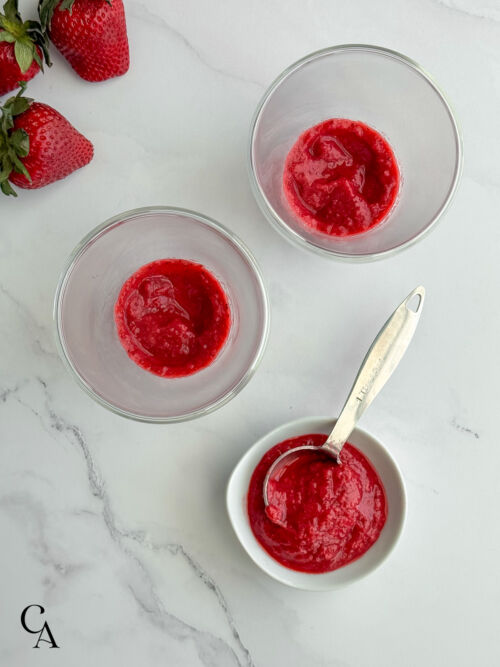 Overlay of two glasses with strawberry purée in the bottom, and more in a small bowl with a measuring spoon nearby.