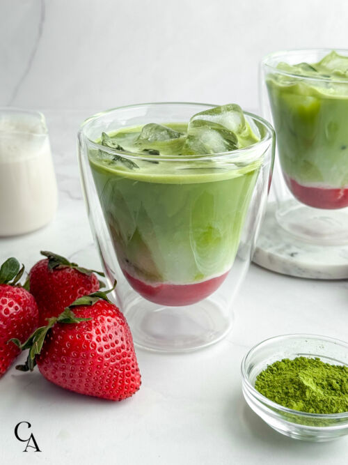 A strawberry matcha with almond milk in the background and fresh berries on the side.